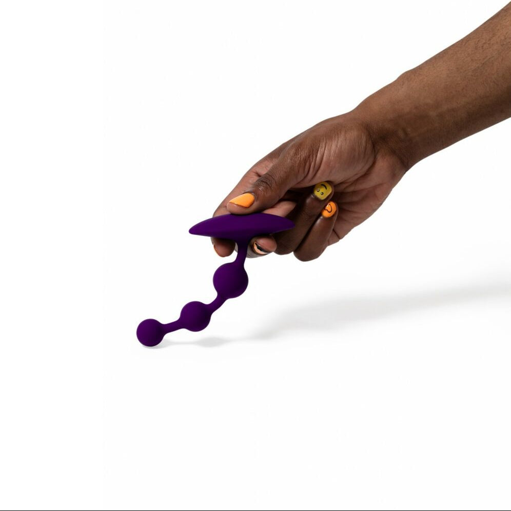 Hand holding a purple flexible anal beads and against a white background