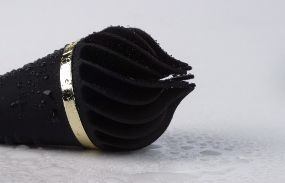 Black waterproof clitoral stimulator with gold trim on a light gray background