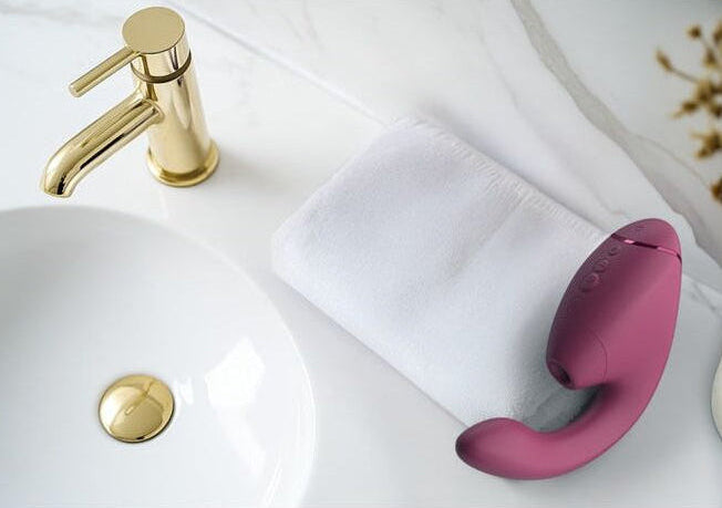gold faucet handle and pink sexual wellness device on a white sink with gold faucet