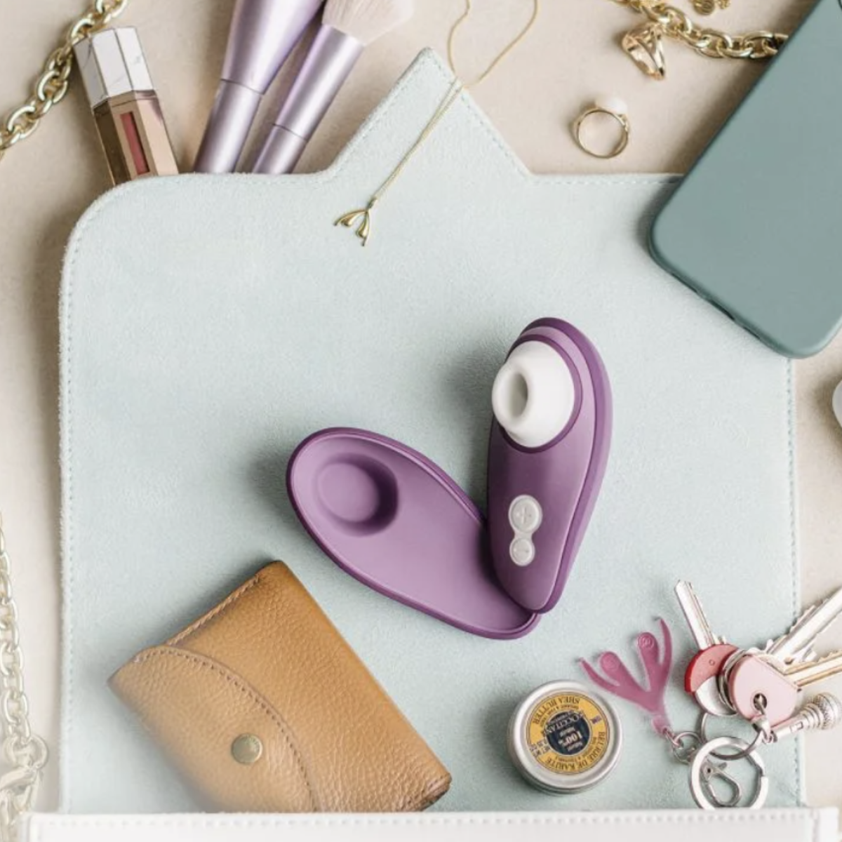 Purple and white sexual wellness  erotic device on a light blue surface with women's accessories around