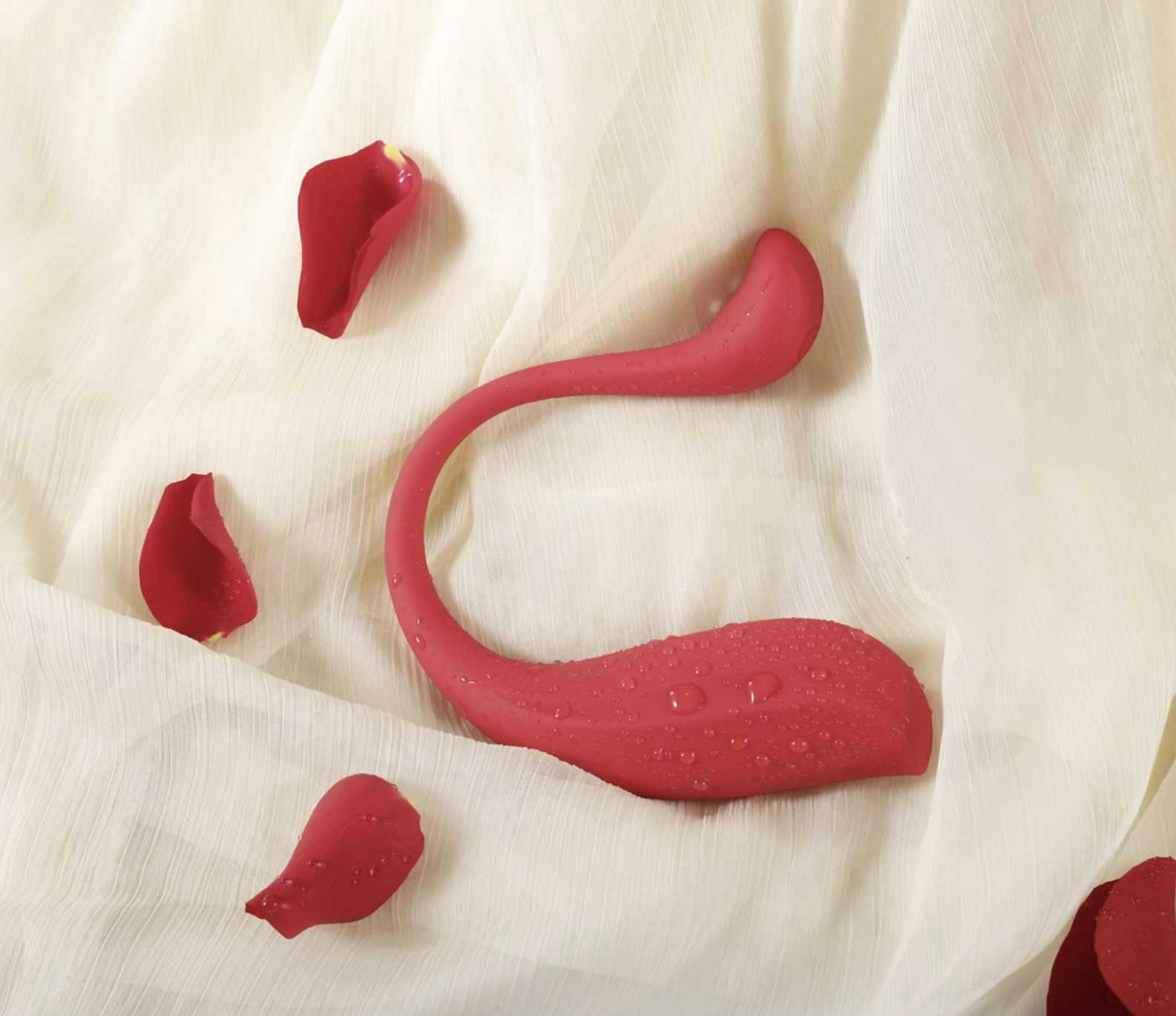 Red silicone adult product on a white fabric background with red petals.
