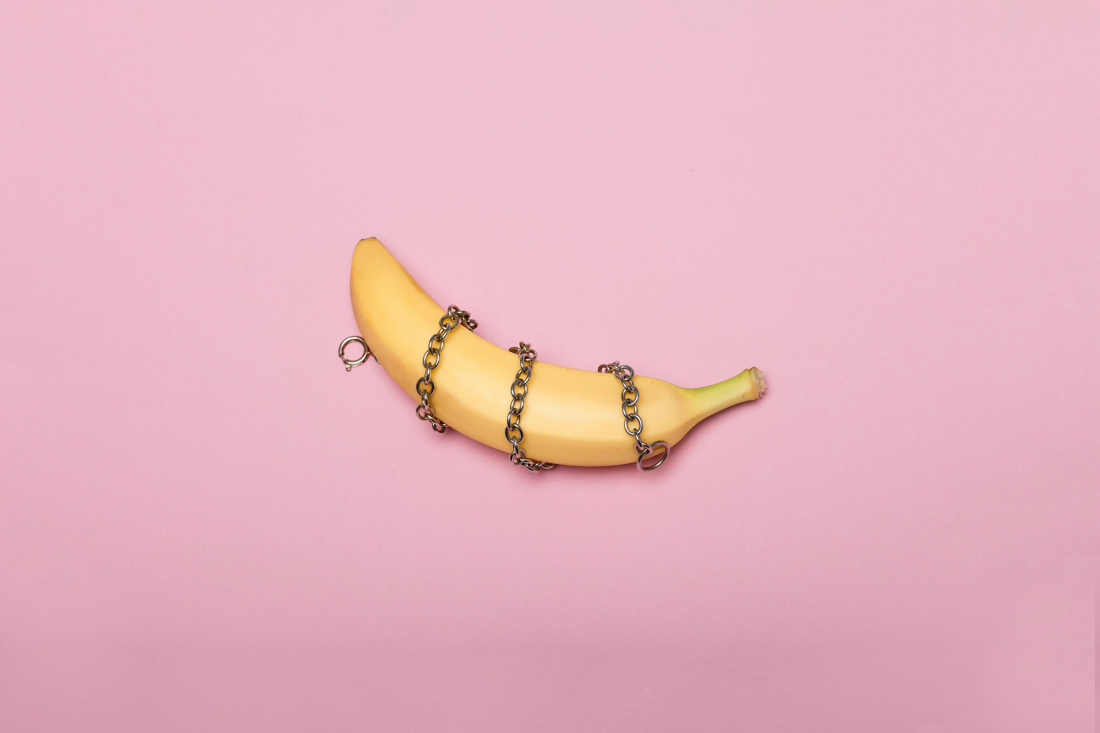 big yellow banana in bondage chains on a pink background