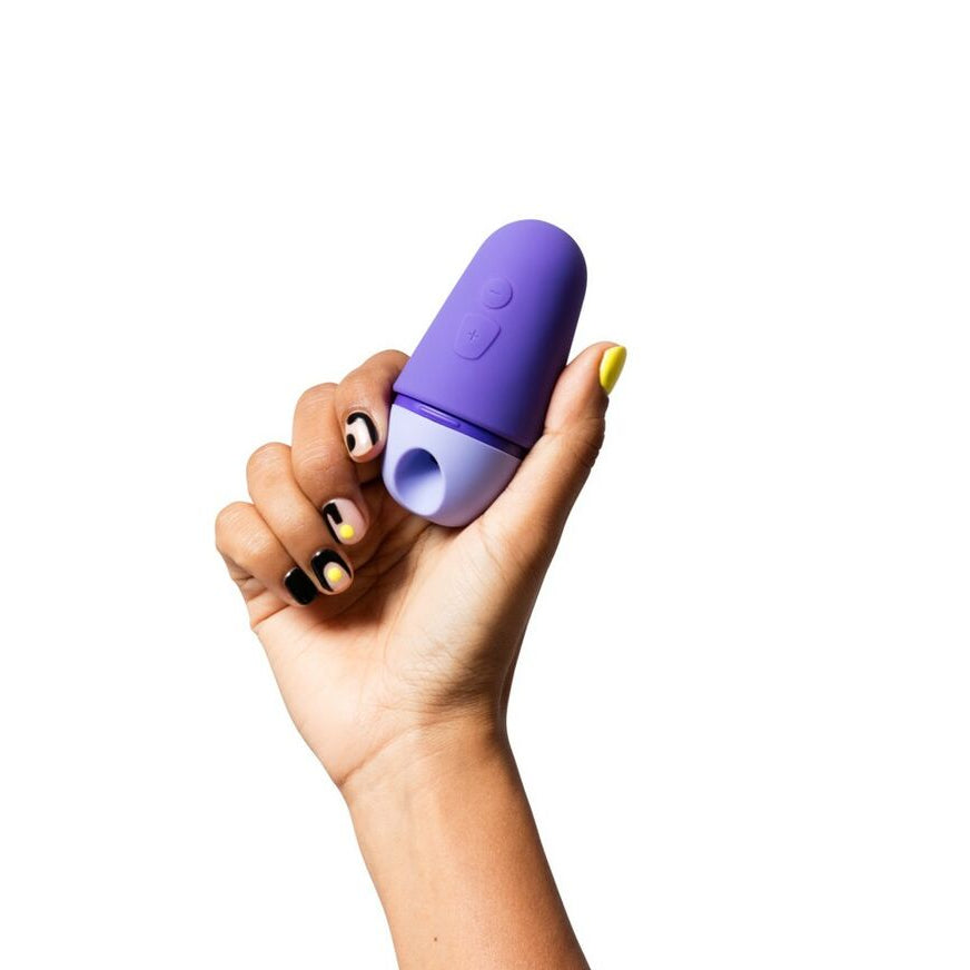 Hand holding a purple and white air suction pleasure toy against a white background
