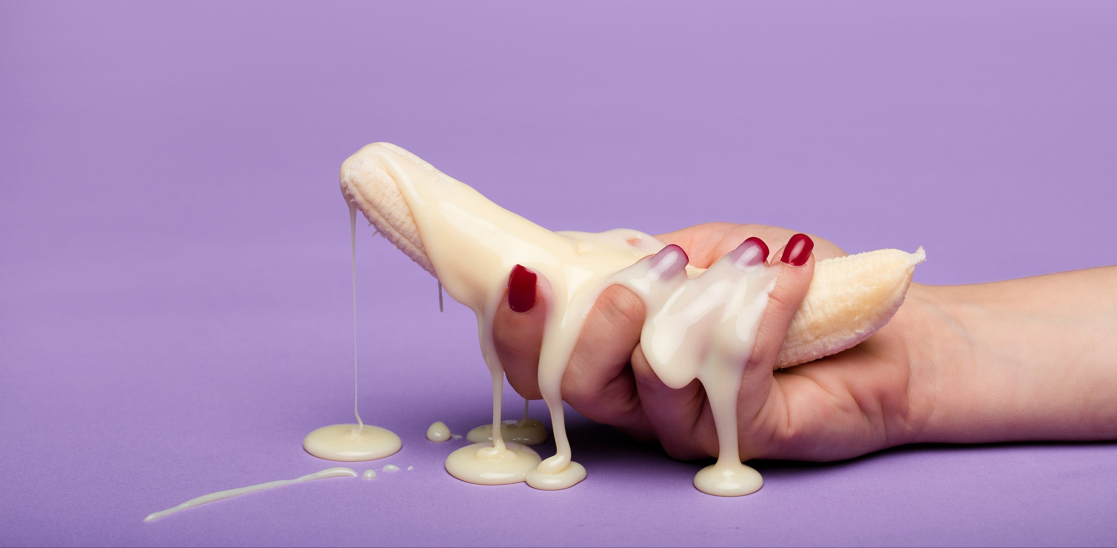 Hand holding a banana with white cream on a purple background