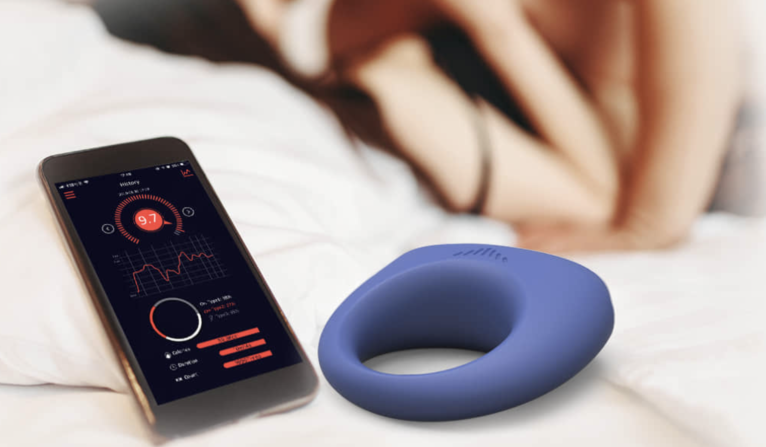 Smartphone with app interface and a blue silicone ring on a bed.