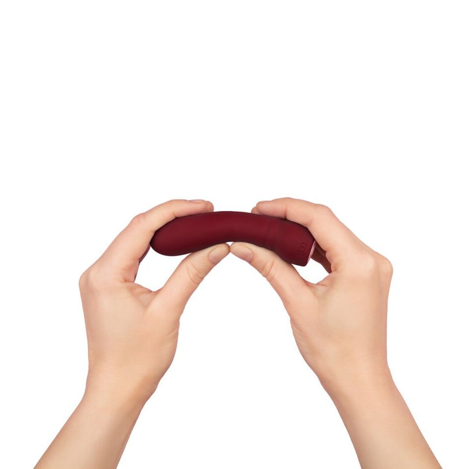 Hands holding a maroon sexual wellness object against a white background