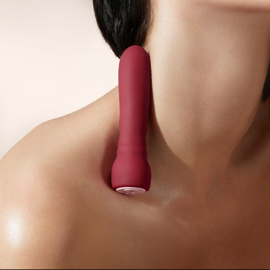 Red intimate massager being used on a person's neck against a neutral background