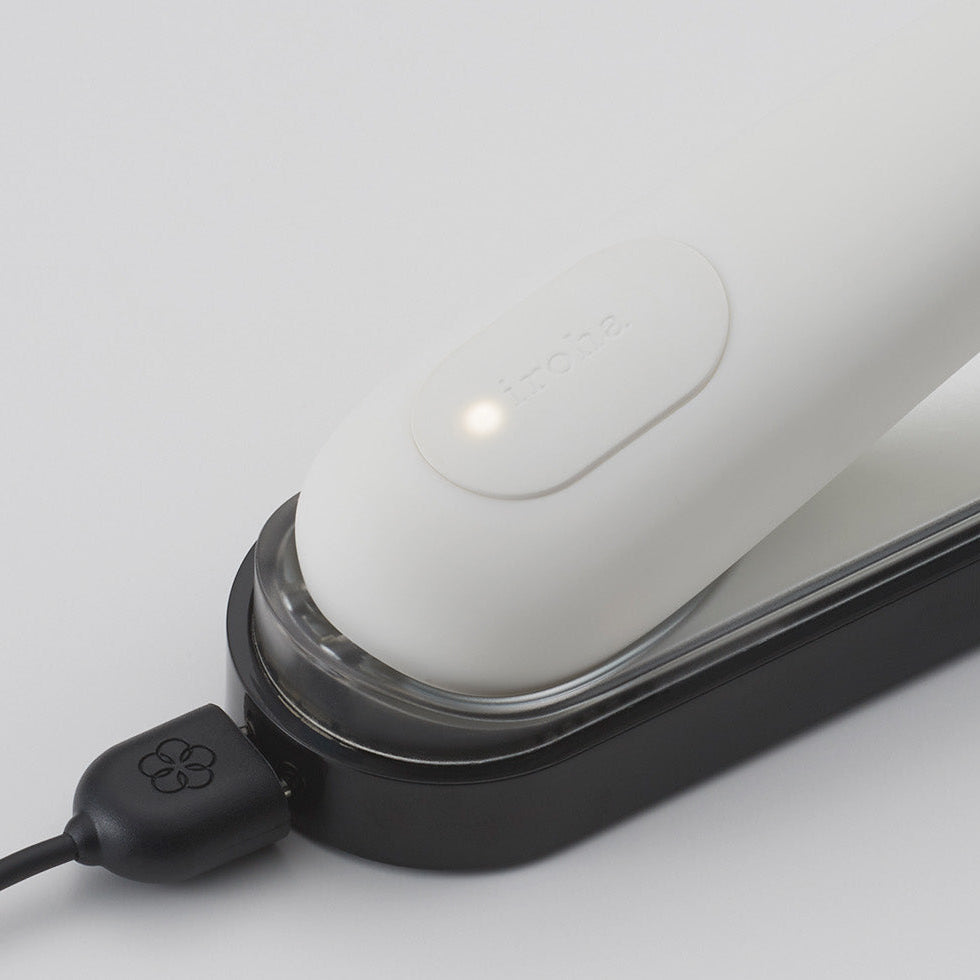 Close-up of a rechargeable white vibrator with a black usb cable on a light gray background