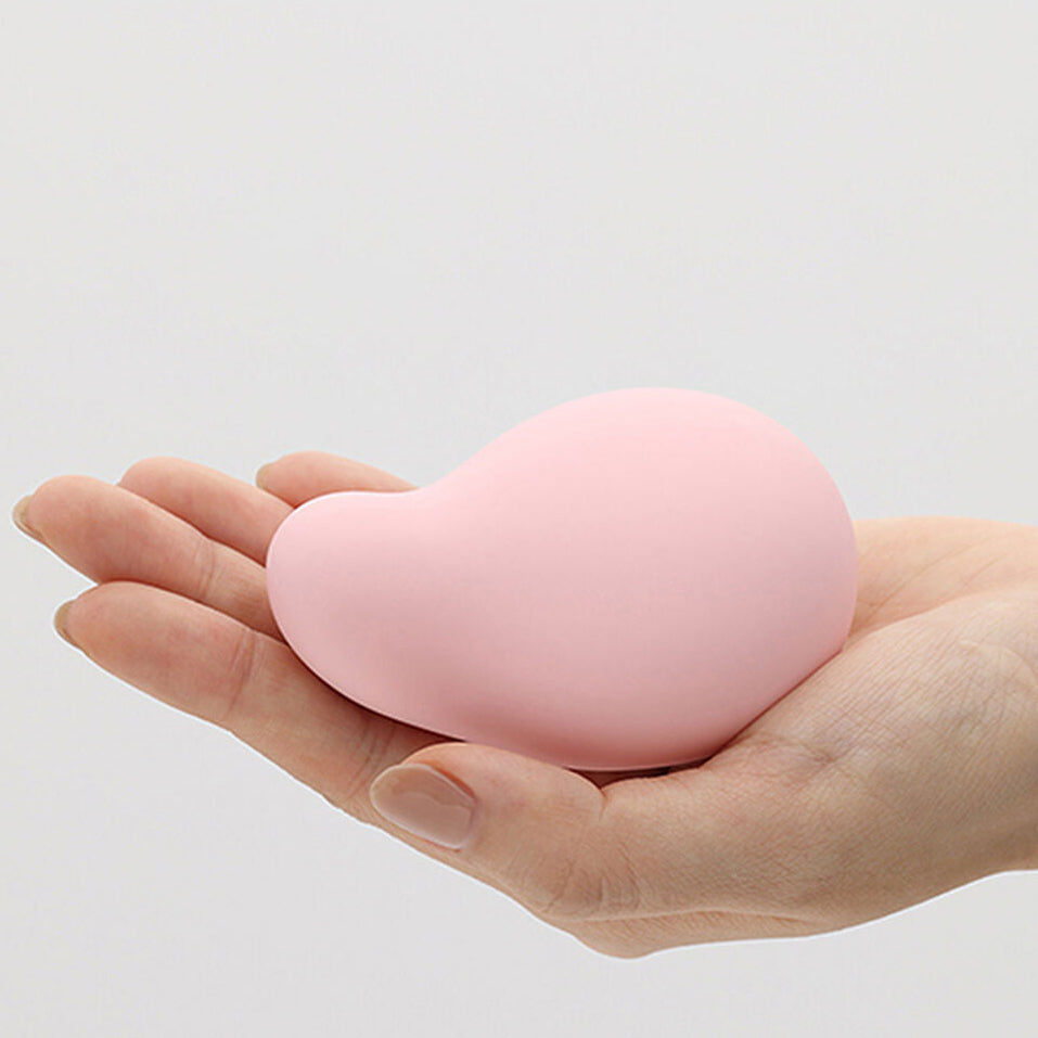 Pink heart-shaped silicone vibrator held in a hand against a light gray background