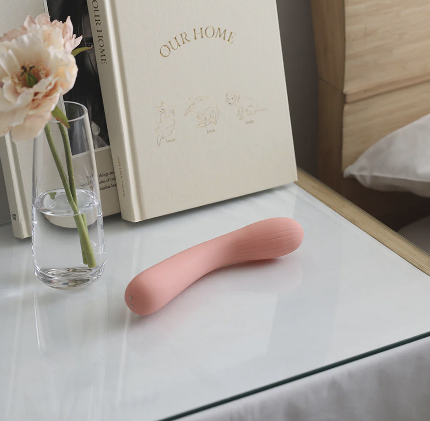 Pink silicone intimate massage wand on a glass table with a vase of flowers and books in the background.