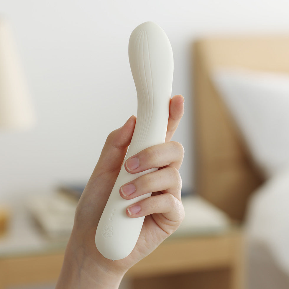 Hand holding a white luxury vibrator in a bedroom setting