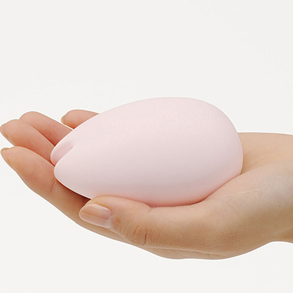 Pink egg-shaped lay-on vibrator for women held in a hand against a white background