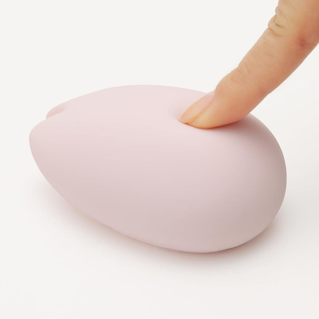 Pink heart-shaped soft silicone vibrator with a finger pressing on it against a white background