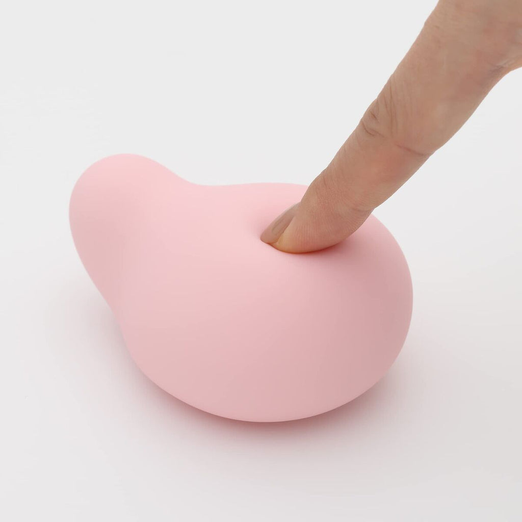 Heart-shaped pink sexual wellness device with a finger pressing on it against a white background