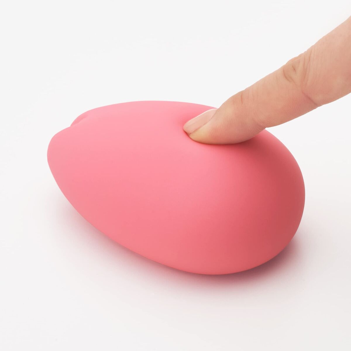pink adult pleasure toy being pressed by a female finger over a white background