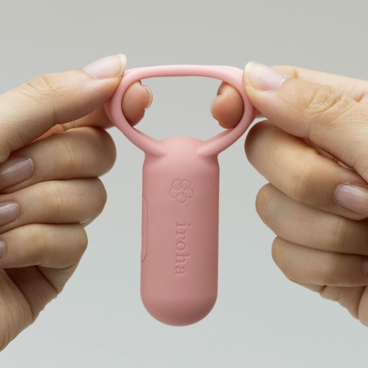 Pink finger vibrator with 'iroha' branding held between two hands against a gray background