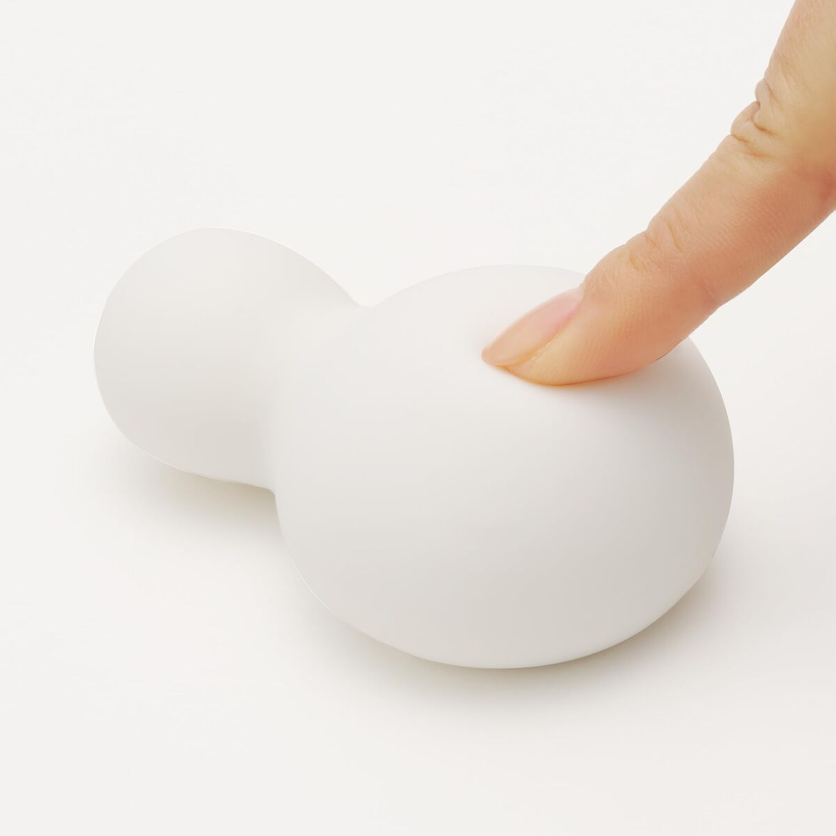 soft silicone white sexual wellness device being pushed with a female finger over a white background