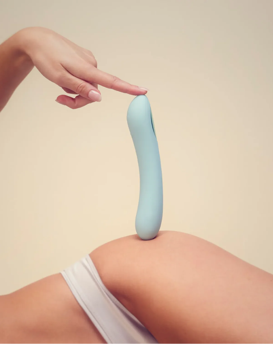 Light blue silicone dildo held by a hand against a beige background