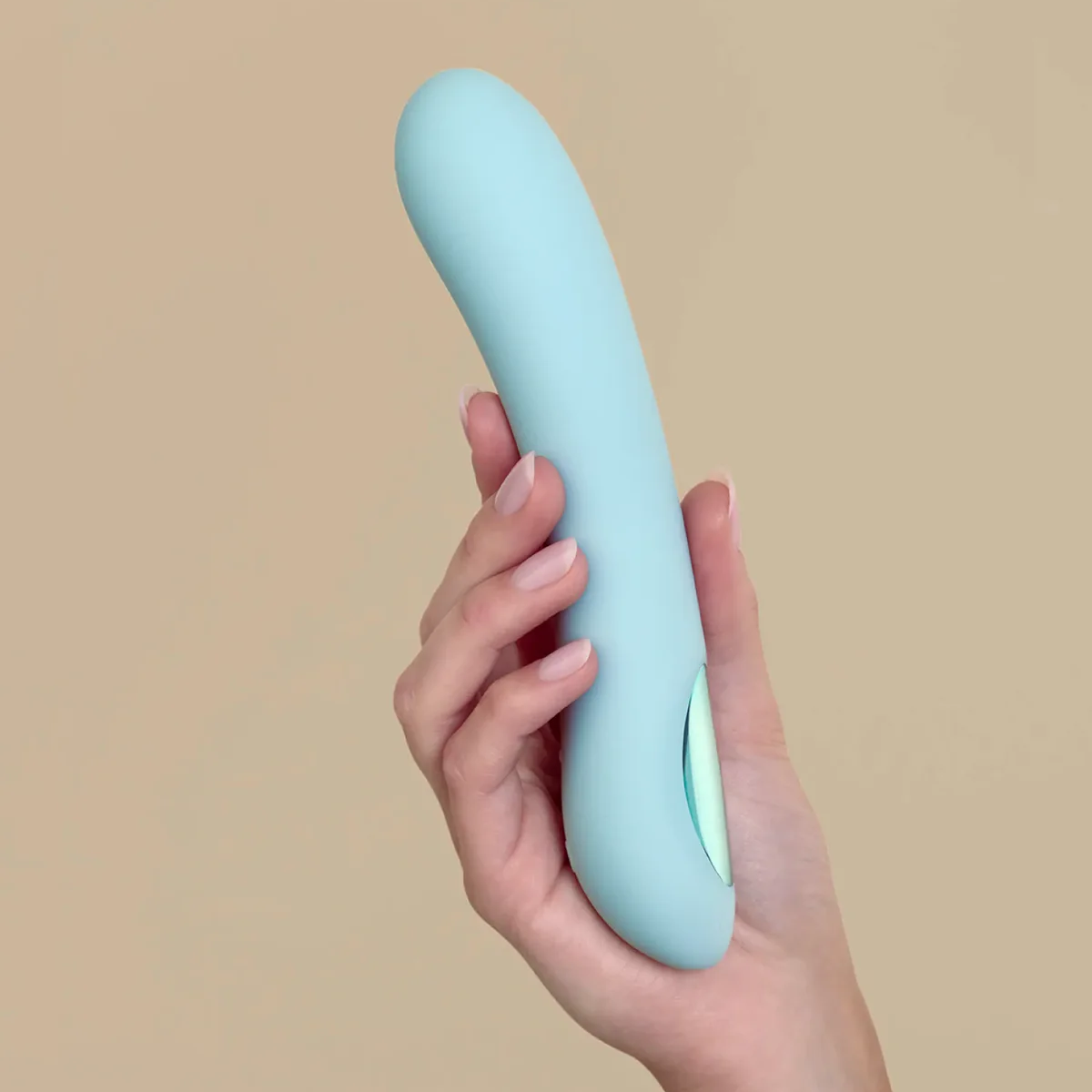 Hand holding a light blue pleasure device against a beige background