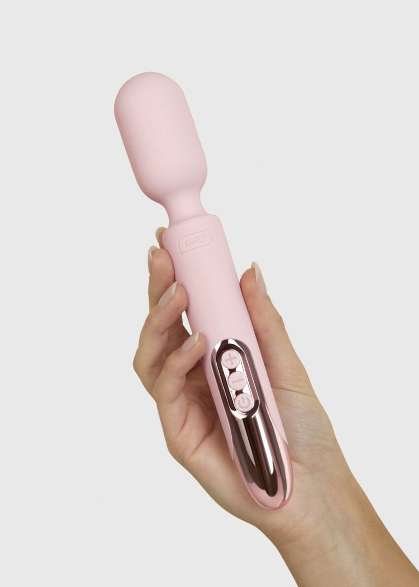 hand holding a rose gold and pink personal massager over a grey background