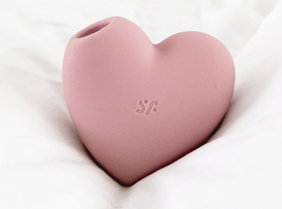 pink heart shaped silicone toy with brand logo 'Satisfyer' on white sheets