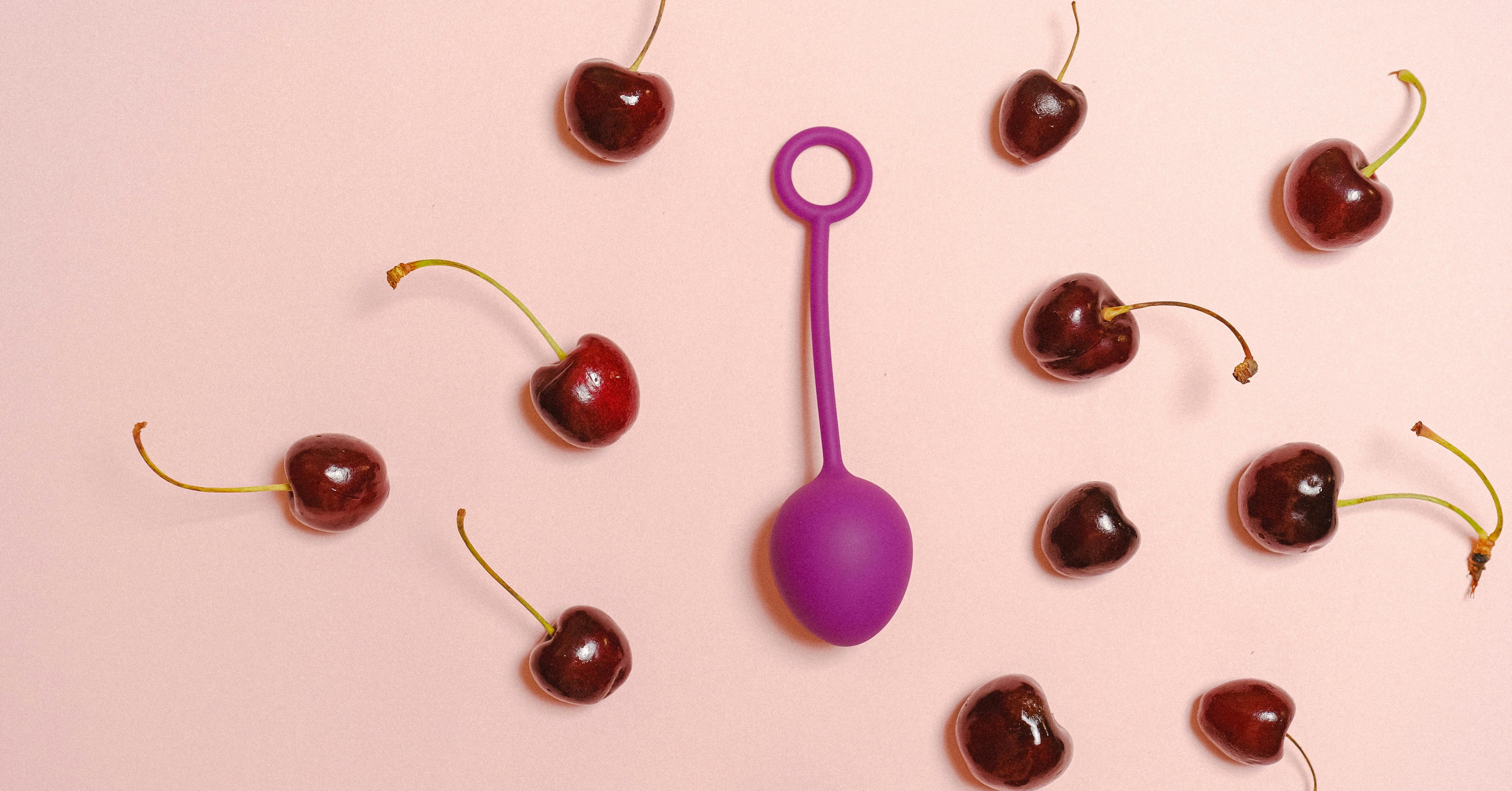 Purple chinese egg vibrator surrounded by cherries on a pink background