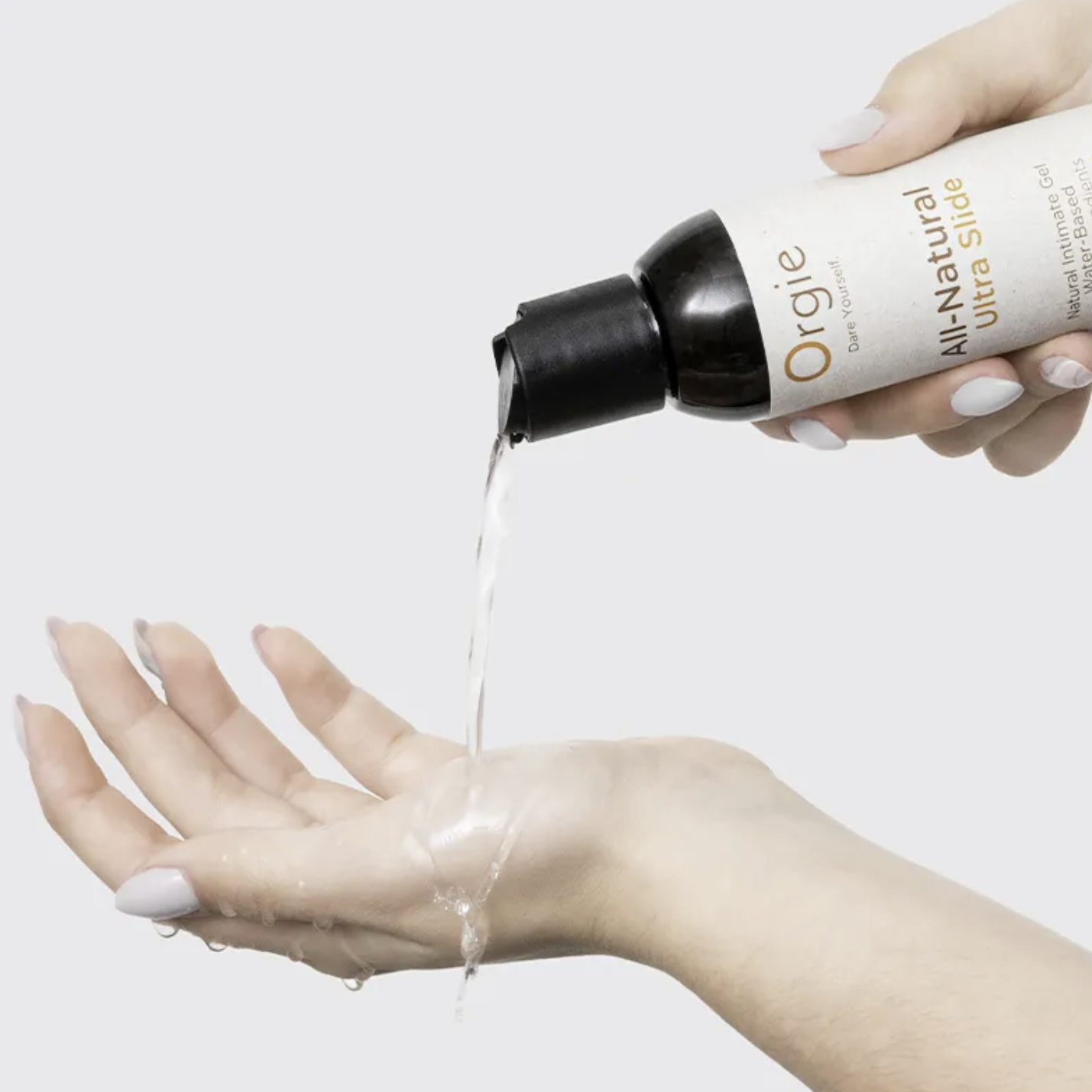 Person pouring a clear liquid from a bottle labeled 'Orgie' natural intimate gel onto their hand against a white background.