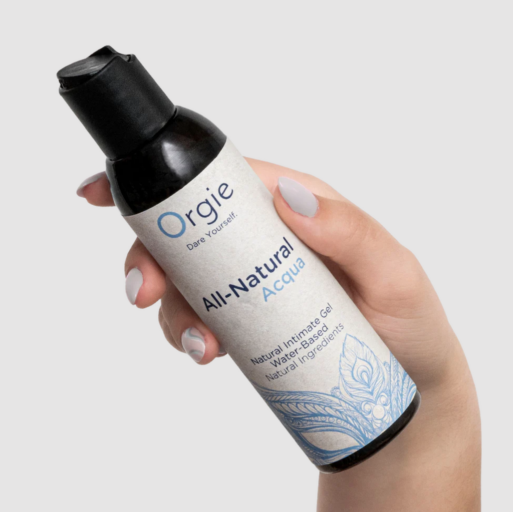 Hand holding a bottle of Orgie All-Natural Acqua personal lubricant product on a light gray background