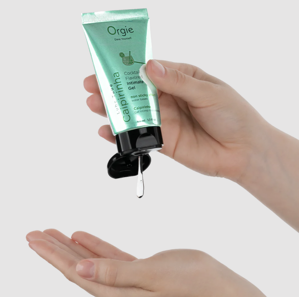 Hand holding a green cosmetic tube labeled 'Orgie' with a clear gel being squeezed onto a palm.