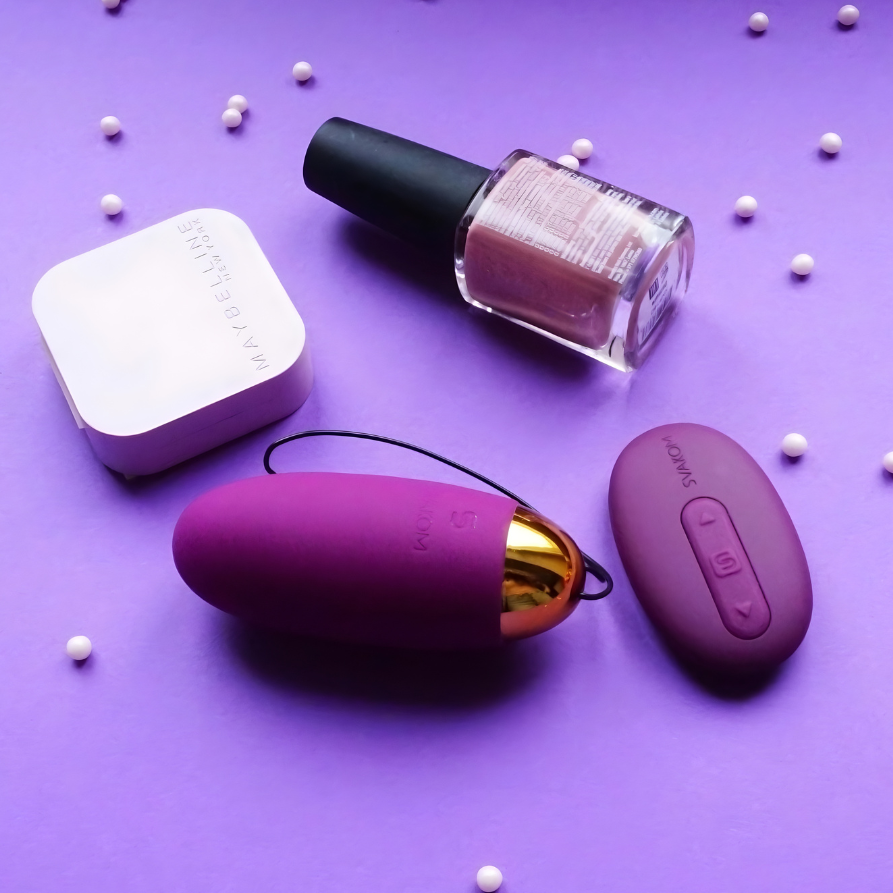 assortments of women's cosmetics and svakom branded purple adult toy on a purple background