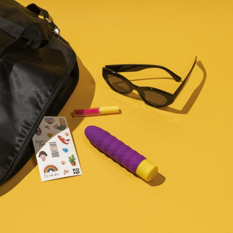 Black bag, sunglasses, and a purple vibrator on a yellow background