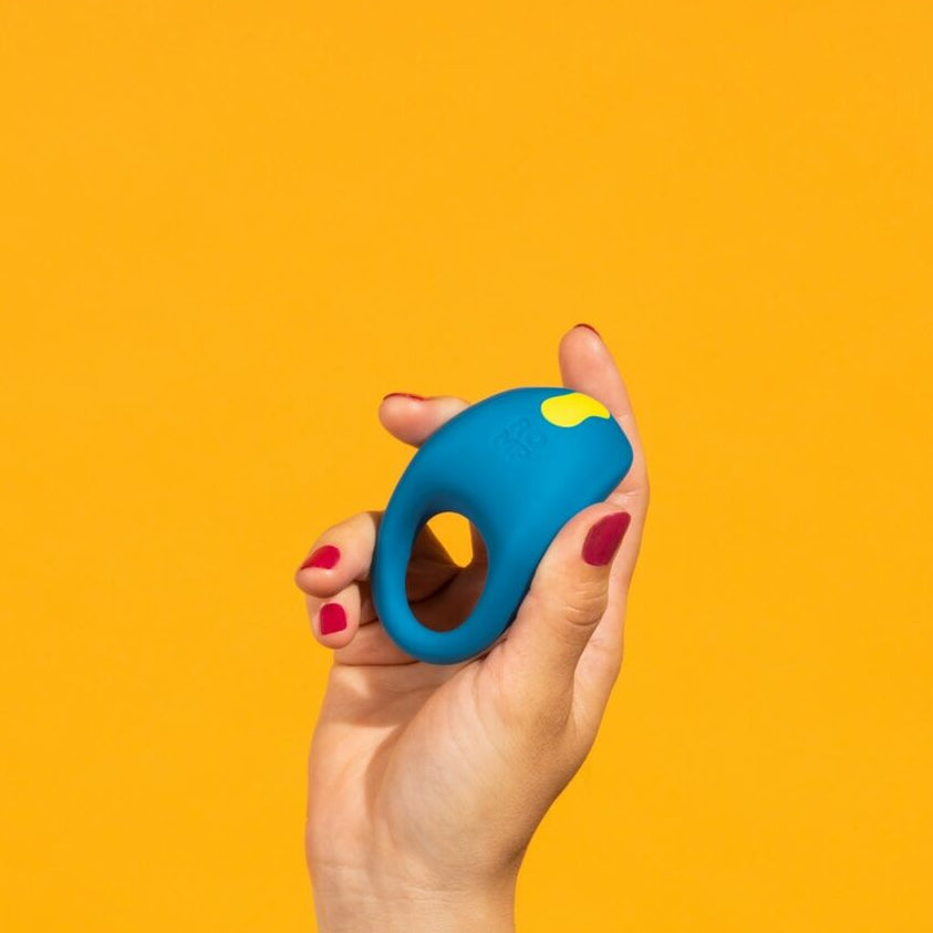 Hand holding a blue and yellow cock ring against a yellow background