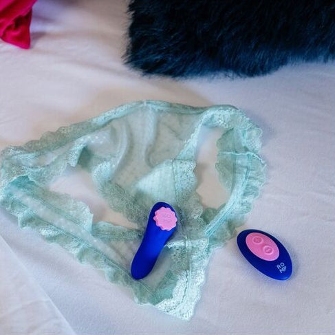 Light green lace underwear with two pink and blue vibrator on a white surface.