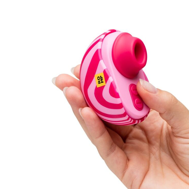 Hand holding a pink and white striped romp clitoral stimulator with air pulse object against a white background