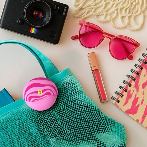 Green mesh bag with colorful items including a romp spin clitoral vibrator camera, sunglasses, and bottle on a white background