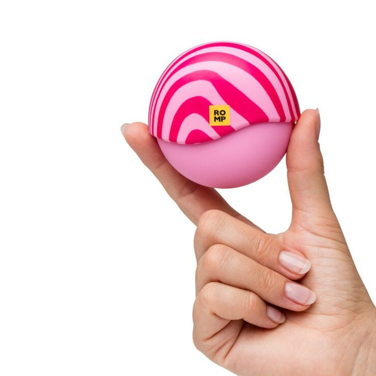 Pink and white striped ball shaped sexual wellness device held in a hand on a white background