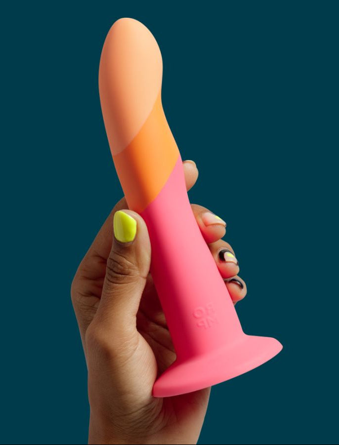 Hand holding a pink and orange silicone dildo product against a dark blue background