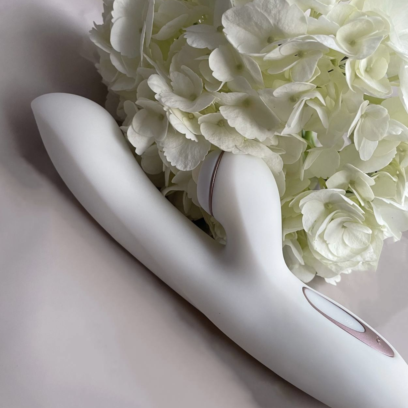 White rabbit massager with pink accents on a light gray background with white flowers.