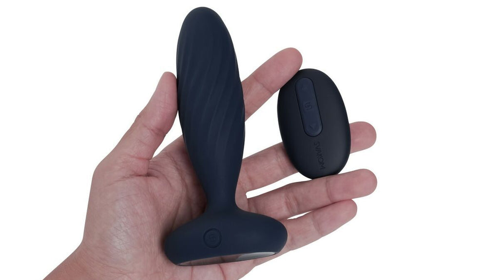 Black silicone butt plug with remote control on a hand against a white background