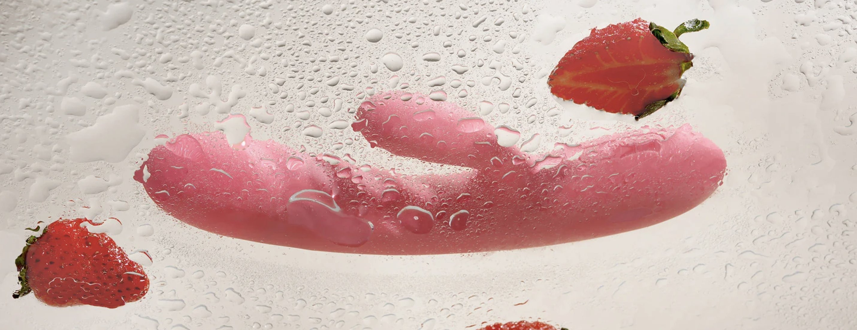 Pink silicone rabbit vibrator with bubbles on a textured white background with strawberries.