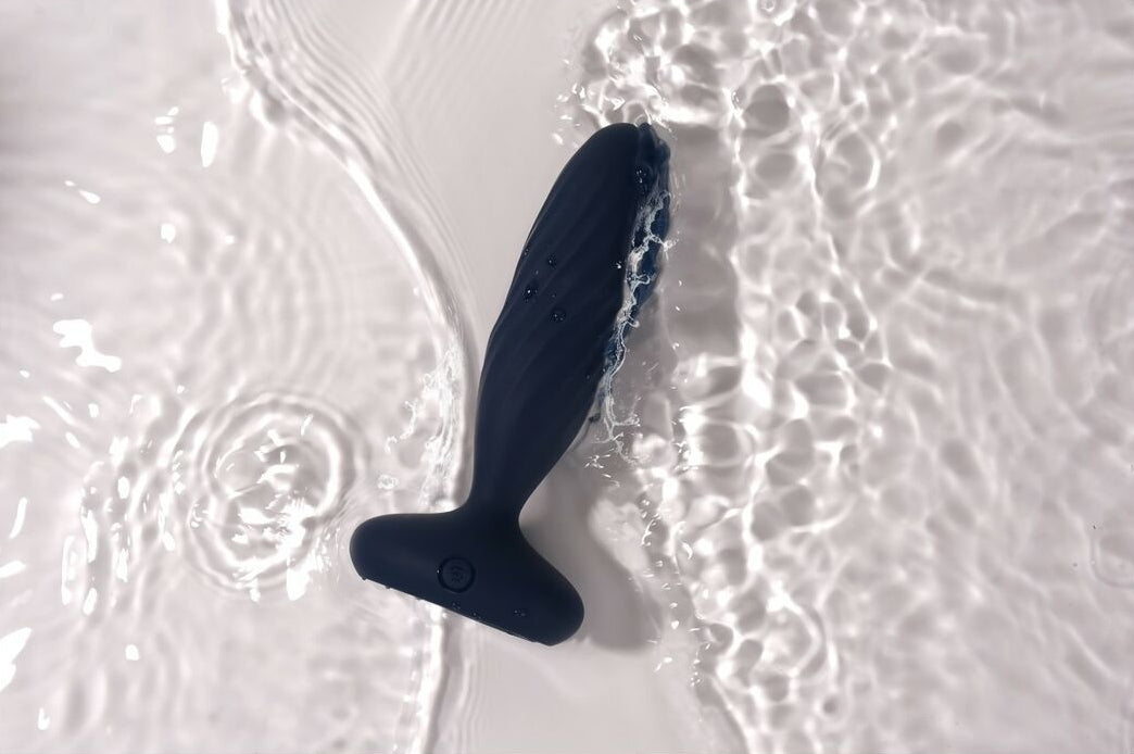 Black silicone butt plug floating on water with ripples