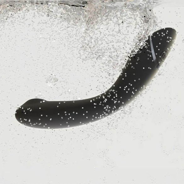 Black silicone vibrator floating in water with bubbles on a white background