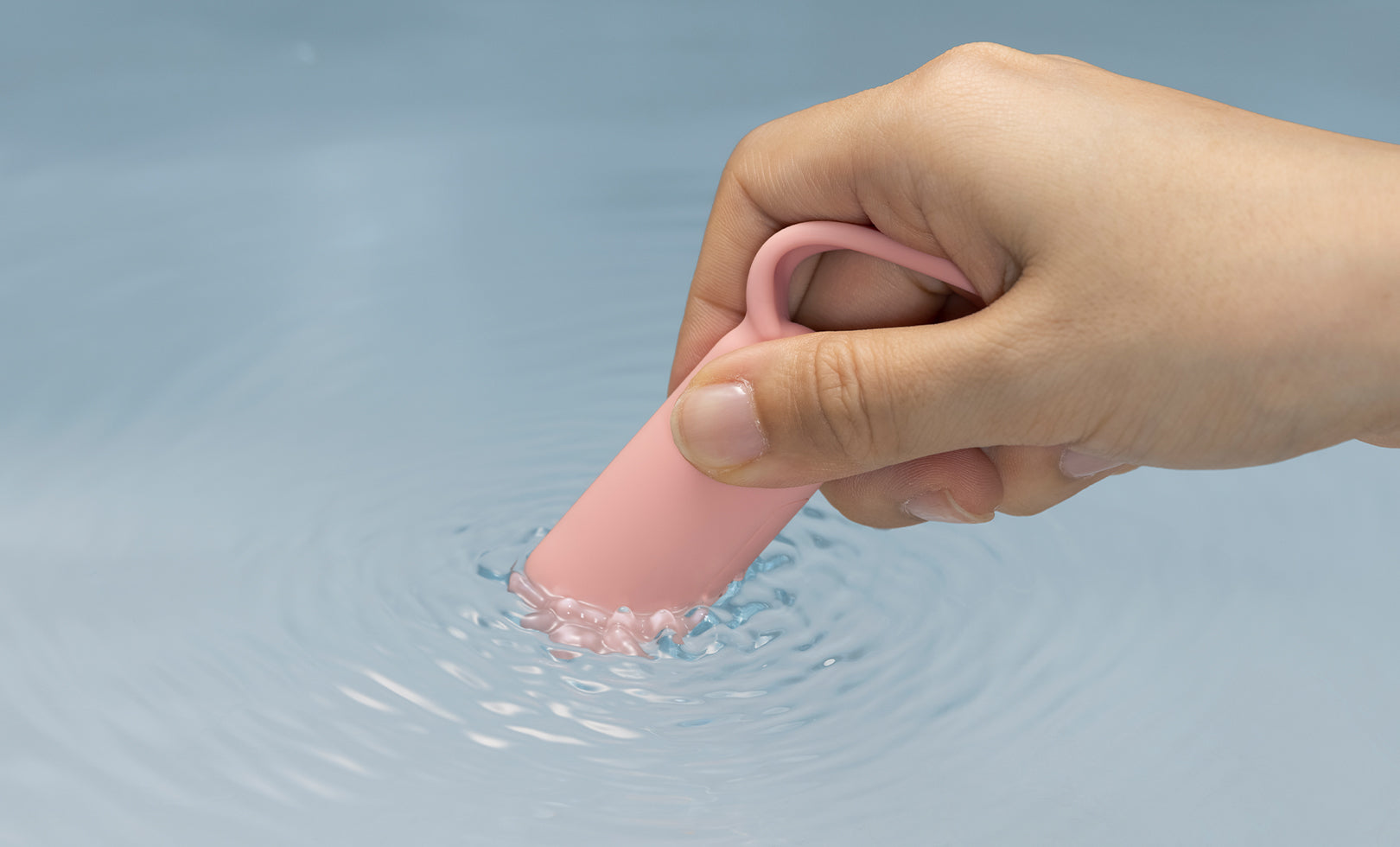 Hand holding a pink silicone pleasure device in water with a blue background