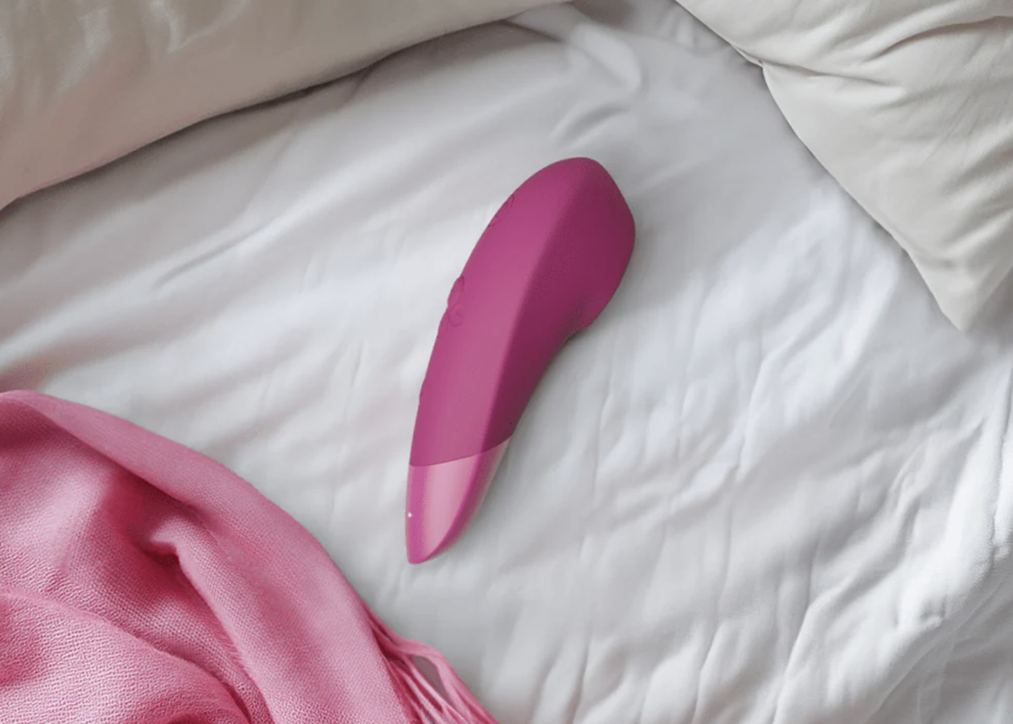 pink adult erotic device on white bedsheets