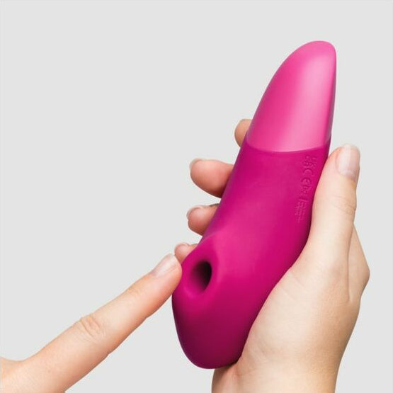 Pink pleasure toy held in a hand against a white background