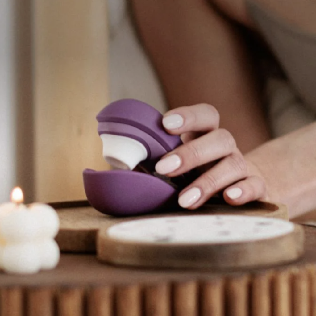 Hand holding a purple and white adult pleasure toy on a wooden surface with a blurred background